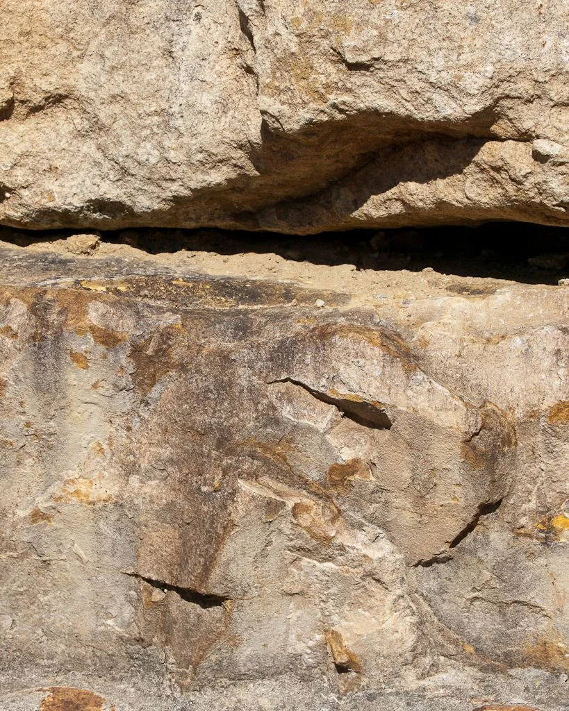 Two courses of weathered sandstone in a dry wall, the blocks cracked and streaked with yellow lichen